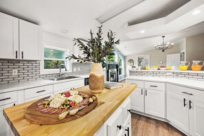 A modern kitchen with white cabinets, a wooden countertop, and a central island with a charcuterie board. - Spacious 5-bed house-hot tub-fire pit-theater rm-game rm-min to Dells attraction (Wisconsin Dells)