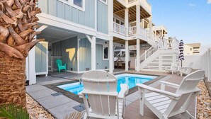 A pool area with white deck chairs and a small pool, surrounded by a two-story building with balconies. - Fall Availability | Steps to Beach | 7 bdrm home (Holden Beach)