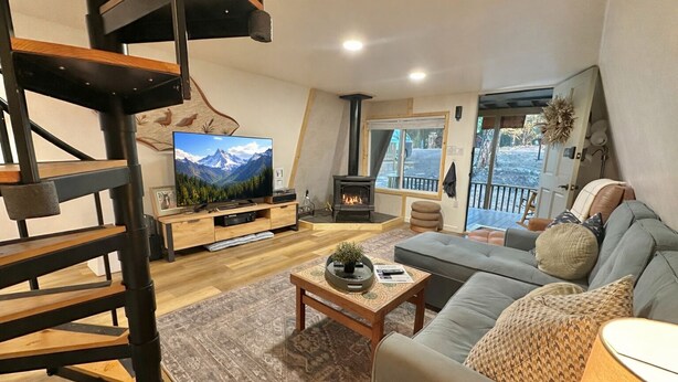 A modern living room with a wooden staircase, a fireplace, a sofa, and a television. - Adventure's Retreat for Trails & Forest Fun! (Overgaard)