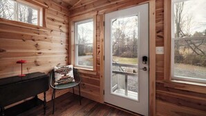 A wooden cabin interior with a bench, a chair, and a door leading outside. - Creekside Mariposa Cottage · Hot Tub & Fire Pit (Berkeley Springs)