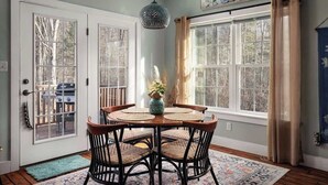 A dining area with a round table, chairs, and a hanging light fixture. - Creekside Mariposa Cottage · Hot Tub & Fire Pit (Berkeley Springs)