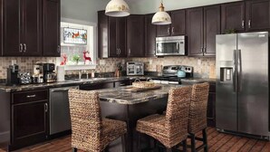 A modern kitchen with dark cabinets, stainless steel appliances, a central island with bar stools, and pendant lighting. - Creekside Mariposa Cottage · Hot Tub & Fire Pit (Berkeley Springs)