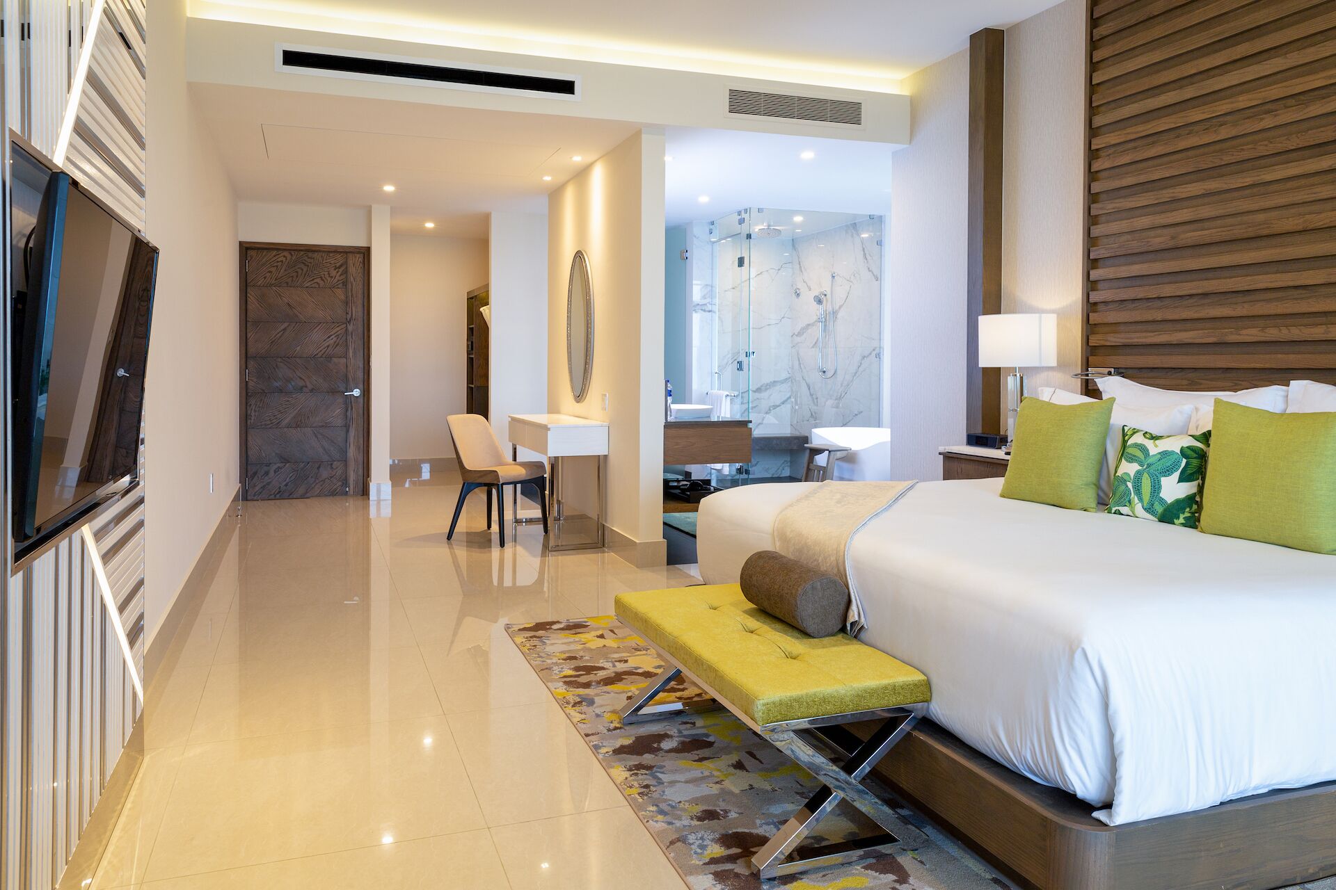Quarto de hotel moderno com cama, mesa de cabeceira, luminária e vista para o banheiro.