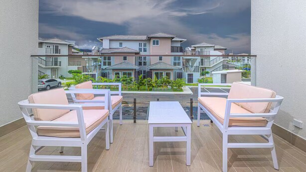 Un balcon doté de mobilier blanc, d’une table en verre et offrant une vue sur des immeubles à plusieurs étages.