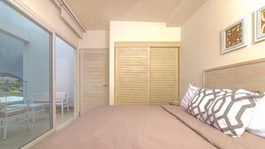 Une chambre à coucher comprenant un lit, une porte-fenêtre coulissante donnant sur un balcon, une armoire en bois et deux éléments décoratifs fixés au mur.
