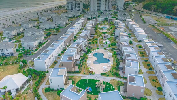Una zona residencial costera con modernos edificios de apartamentos, una piscina central y una playa al fondo.
