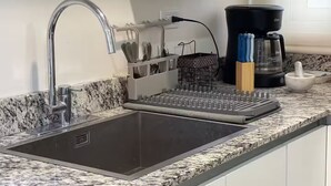 Una cocina con encimera de granito, pileta de acero inoxidable, cafetera y bloque de cuchillos.