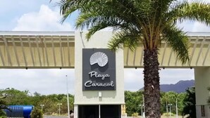 Señal para Playa Caracol, con una palmera y un puente al fondo.