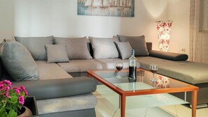 Una sala de estar con un sofá modular, una mesa de centro de vidrio, una planta en maceta y un cuadro en la pared.