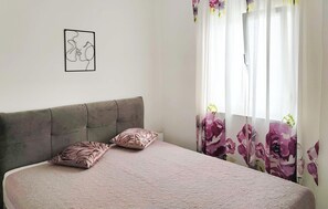A bedroom with a bed, two pillows, a headboard, a wall-mounted picture, and floral curtains. - Cozy apartment in Rogoznica with swimming pool (Rogoznica)