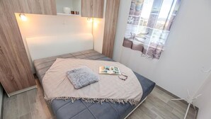 Et kompakt soveværelse med seng, sengebord, et vindue med udsigt og en lampe på væggen.