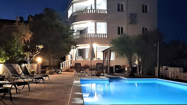 Et udendørs poolområde med liggestole og en bygning i baggrunden.