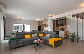 A modern living room with a sectional sofa, a coffee table, and a kitchen area with cabinets and appliances.