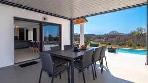 Ein moderner Essbereich im Freien mit Pool, Blick auf die Landschaft und einer überdachten Terrasse.