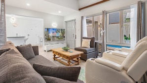 A modern living room with a sofa, armchair, and coffee table. There is a sliding glass door leading to a balcony with plants. - Cuquisastraat 30A (Oranjestad)