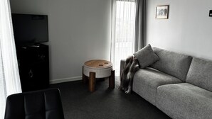 A modern living room with a grey sofa, a small round table, and a television on a cabinet.
