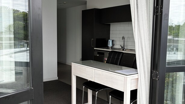 A modern kitchen with a dining area, featuring a glass door, a white countertop, and a black chair.