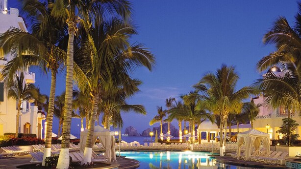 A pool area with palm trees, lounge chairs, and a building with a white facade. - HALF PRICE Fixed Week in Cabo San Lucas (Cabo San Lucas)