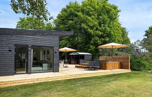 Een modern houten huis met terras, zitgedeelte buiten en een barbecueplek.