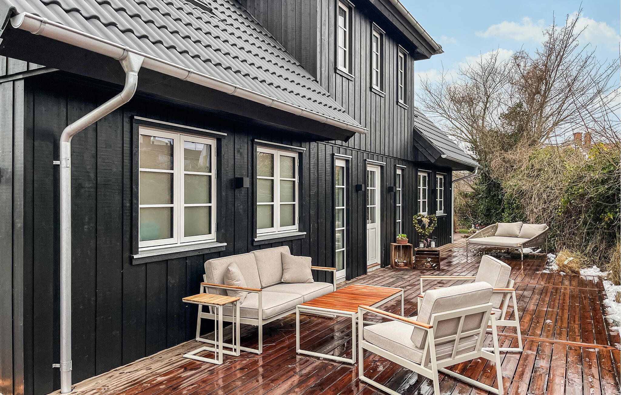 Ein schwarzes Holzhaus mit weiß gefassten Fenstern, eine Terrasse mit Gartenmöbeln und ein Gartenbereich.