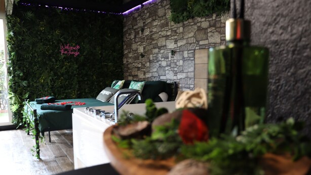 A cozy room with a stone wall, a green sofa, and a wooden table with a flower arrangement. - Jung'Love room - Spa & Private Cinema (Saint-Cyprien)