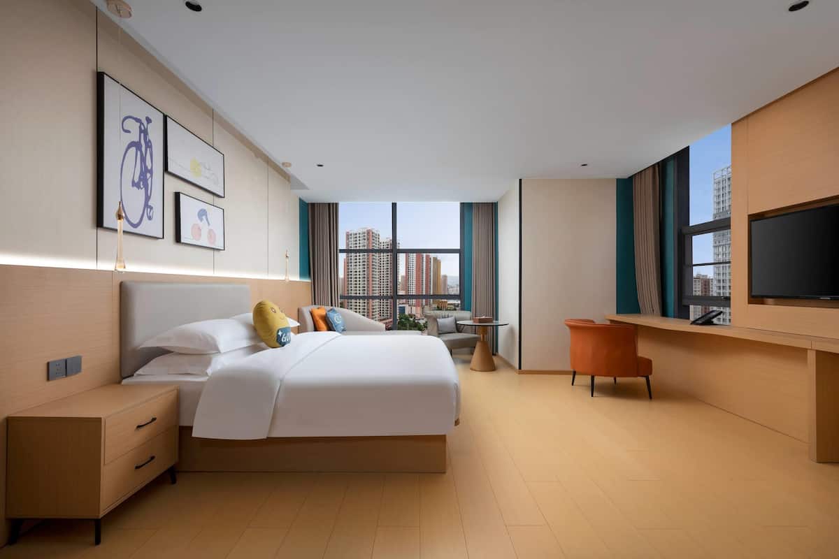 A modern hotel room with a large bed, a desk, a TV, and a city view.