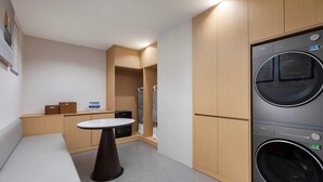 A compact laundry room with a washing machine, a small table, and wooden cabinets. - Baymont Kunming Economic Development Zone (Kunming)