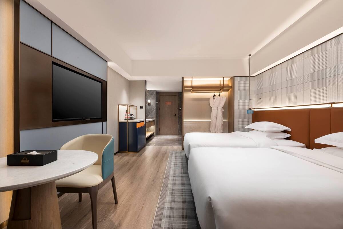Habitación de hotel con cama, televisor, escritorio con silla y bata colgada en la pared.