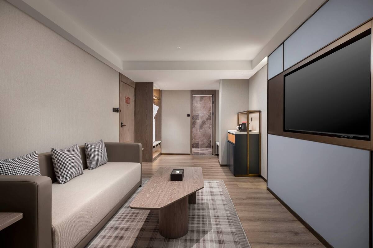Una habitación de hotel moderna con sofá, mesa de centro, televisor de pantalla plana y zona de cocina.