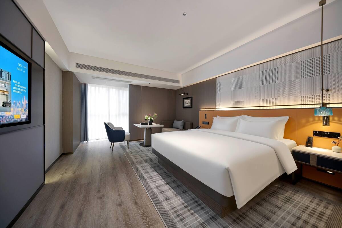 Habitación de hotel con una cama grande, un escritorio, una silla, un televisor y una ventana con cortinas.
