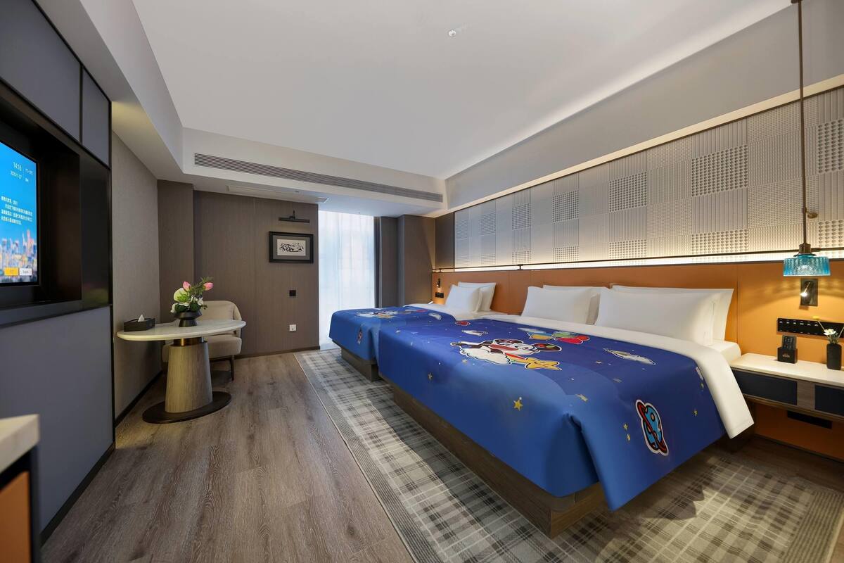Una habitación de hotel con cama, mesita de noche, televisor y un pequeño escritorio con silla.