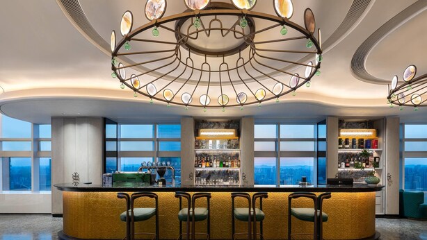 Un bar con diseño circular, taburetes y vistas a la ciudad a través de amplios ventanales.