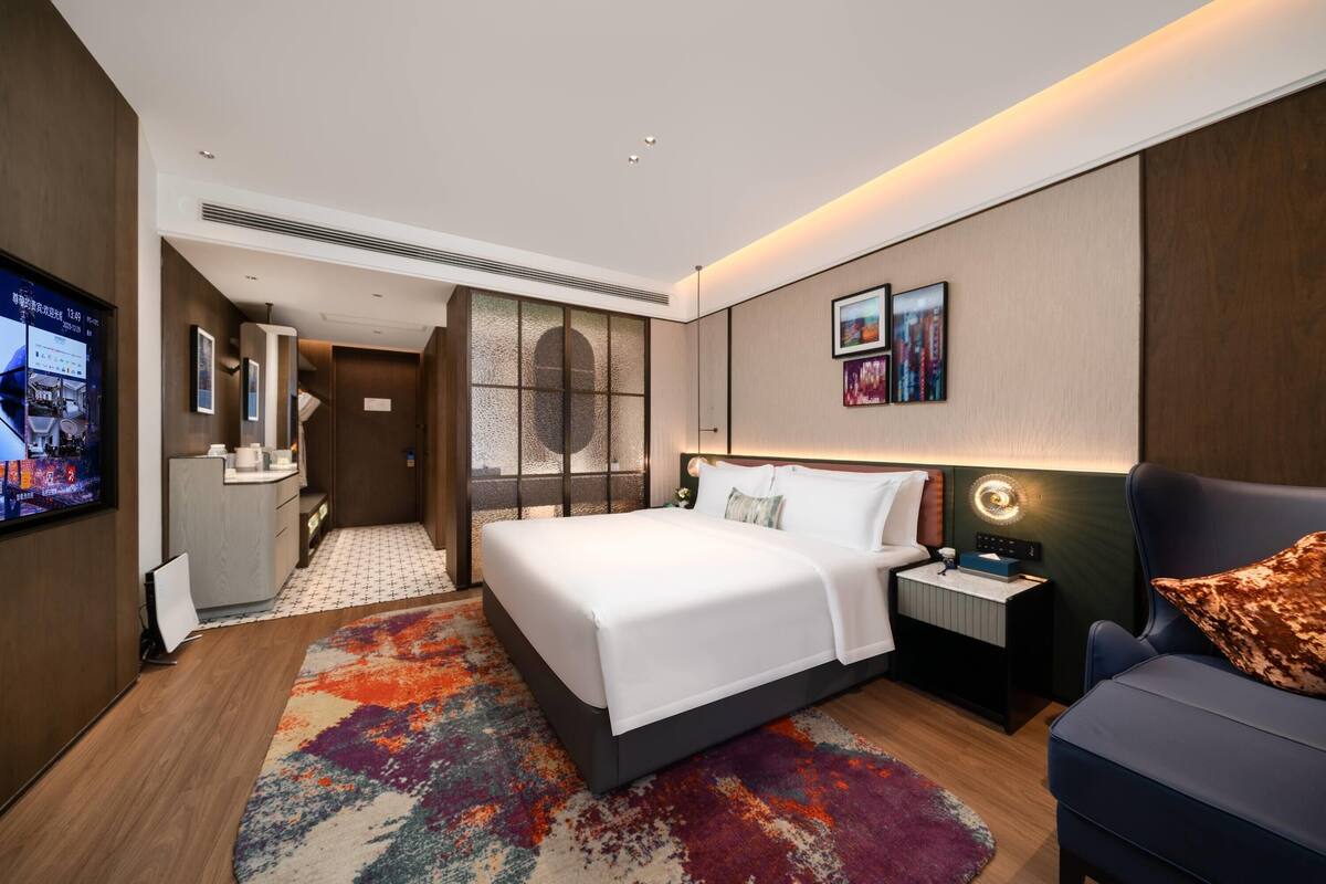 Una habitación de hotel con cama, mesita de noche, televisor y una alfombra colorida.