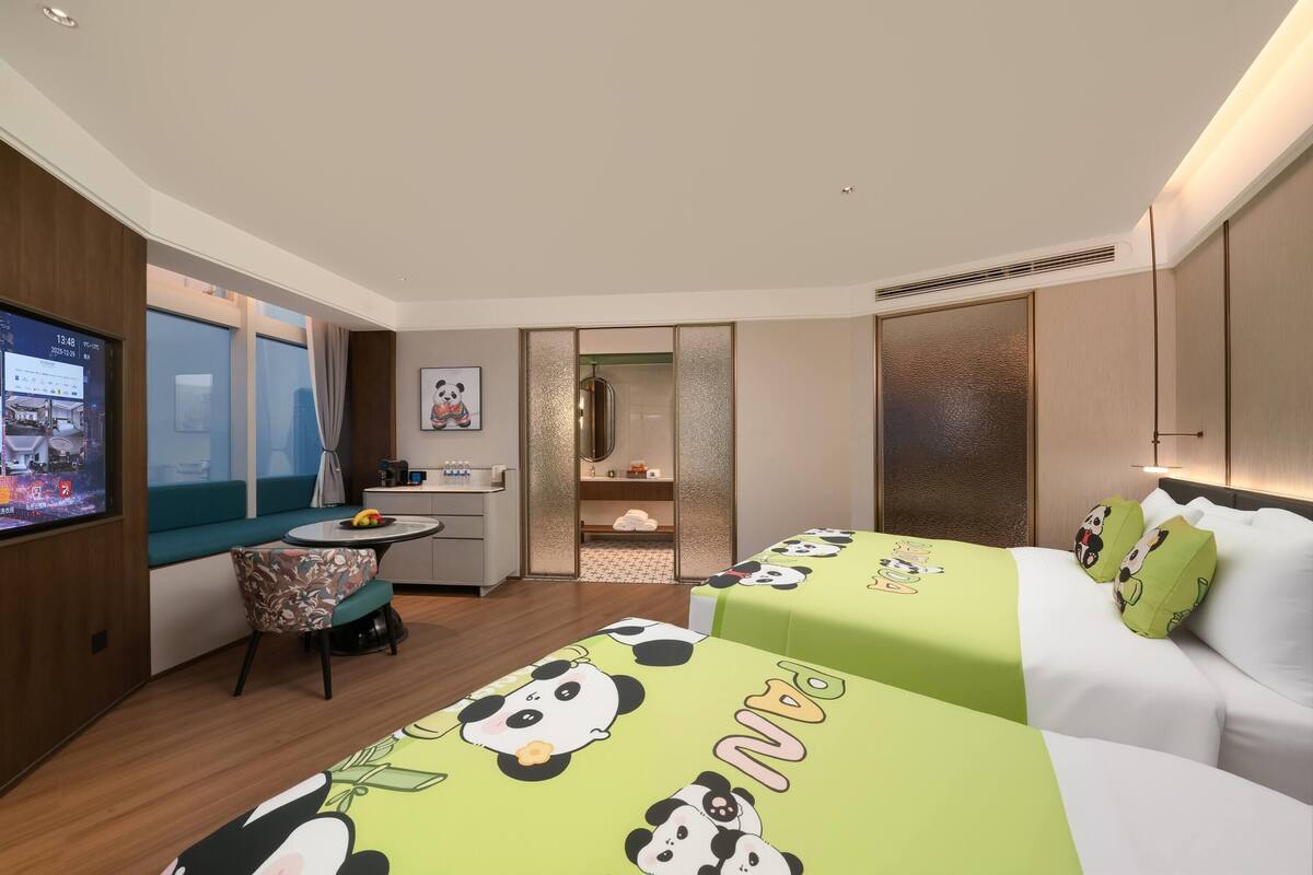 Habitación de hotel con televisión, escritorio, silla, cama con ropa de cama temática de panda y armario.
