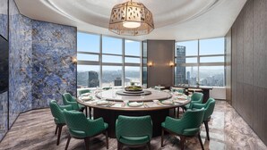 Un comedor moderno con una mesa redonda, sillas tapizadas en verde, un aplique decorativo y vistas a la ciudad a través de grandes ventanales.