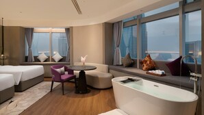 Una habitación de hotel moderna con un ventanal grande, un sofá, una mesa redonda, una bañera y una cama.