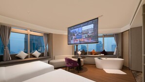 Habitación de hotel moderna con un televisor grande, un sofá, una silla, una bañera y vistas a la ciudad.