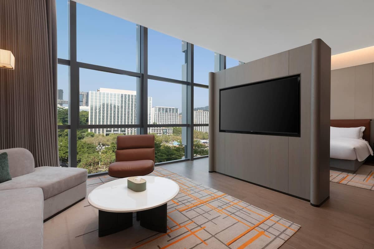 Una habitación de hotel moderna con un televisor grande, asientos cómodos y vistas a la ciudad.
