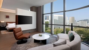 Una habitación de hotel moderna con un ventanal grande, un televisor de pantalla plana, un sofá, una silla y una pequeña mesa.
