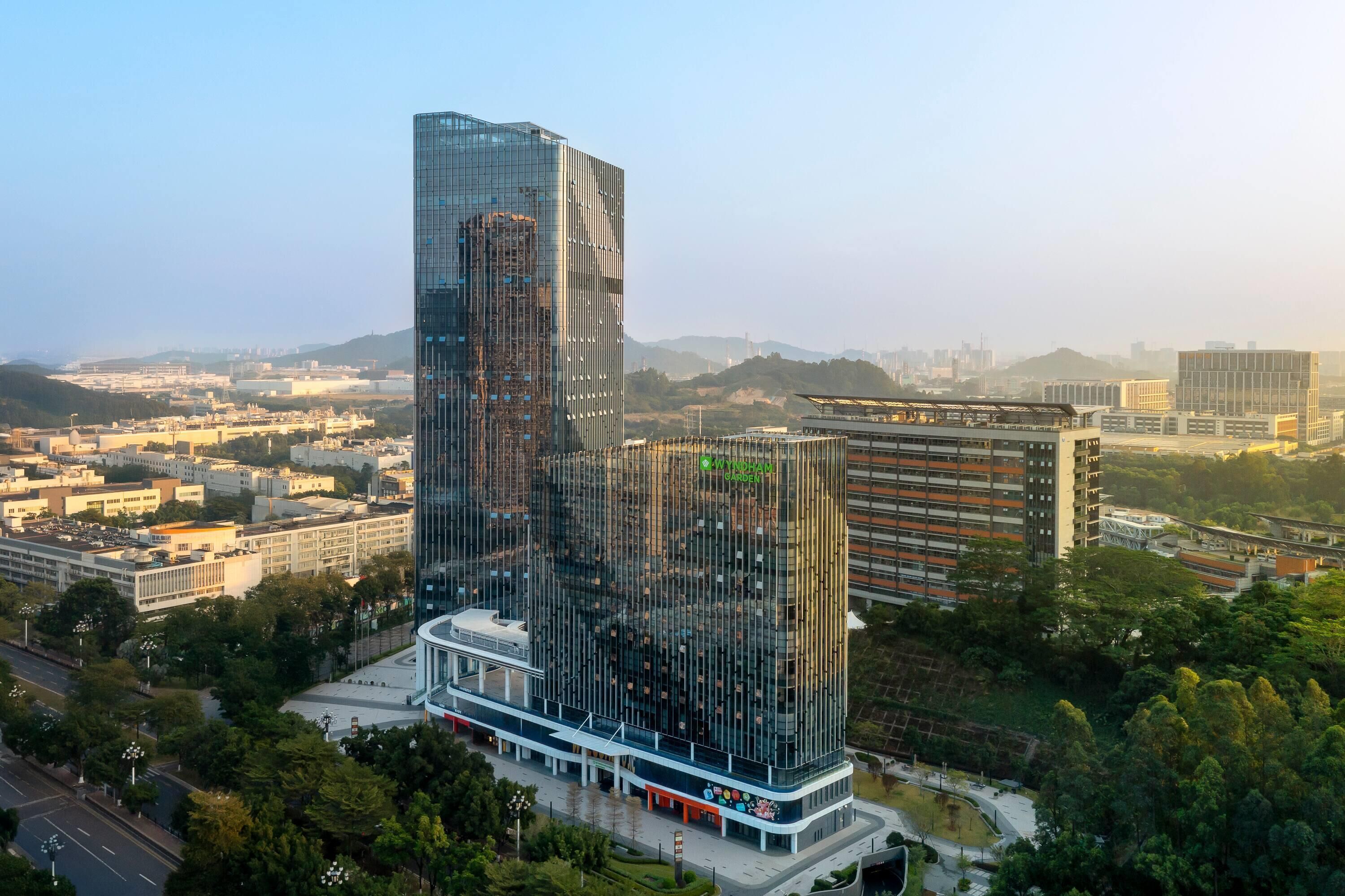 A modern high-rise building with a glass facade, surrounded by other buildings and greenery.