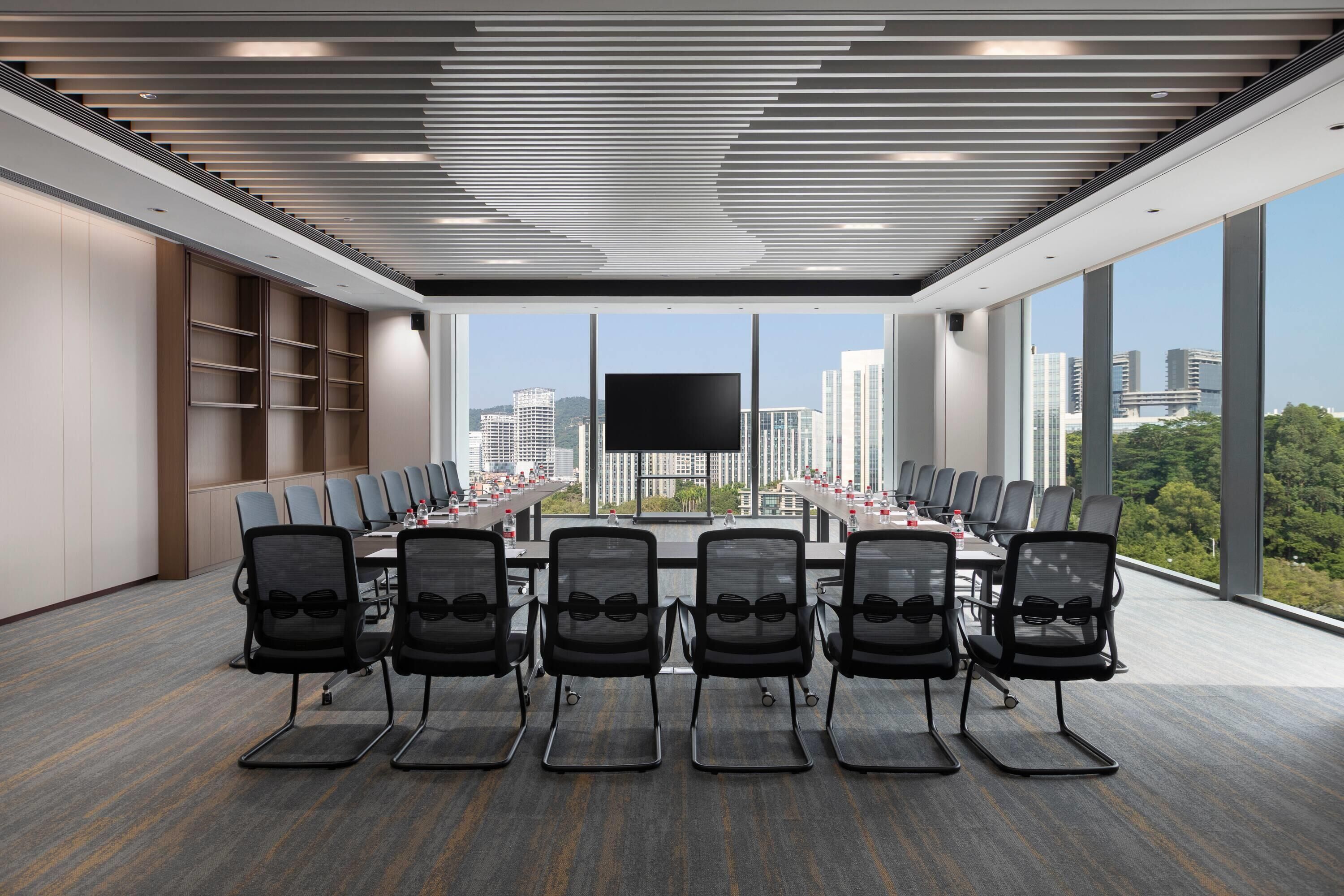 A modern conference room with a large table, black chairs, and a large screen.