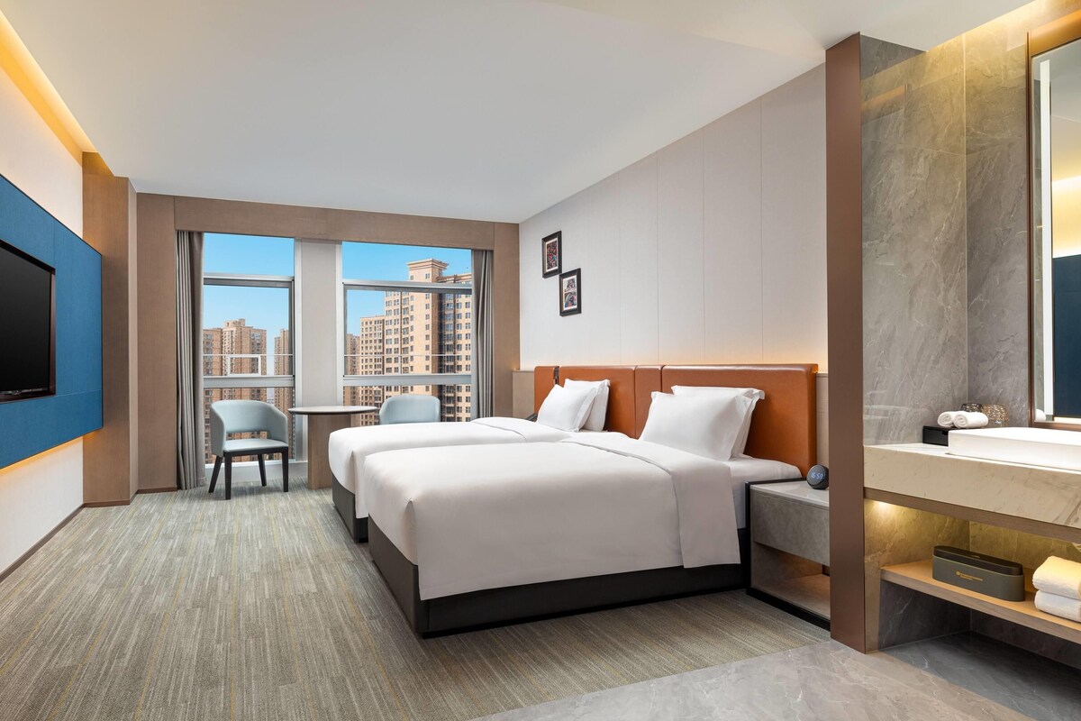 A hotel room with a bed, a desk, a chair, a TV, and a bathroom with a mirror.