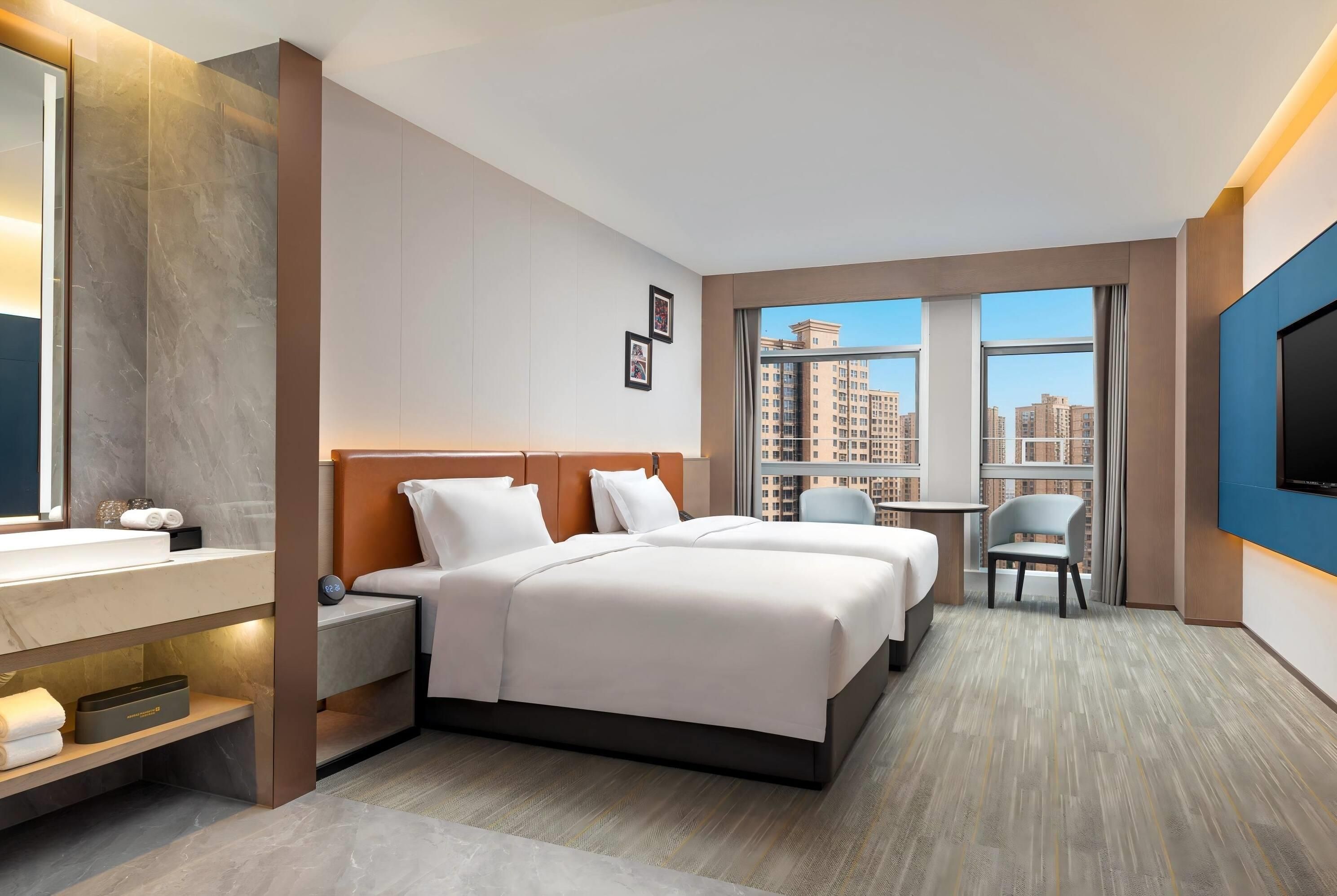 A hotel room with a bed, bedside tables, a TV, a small desk, and a window with a city view.