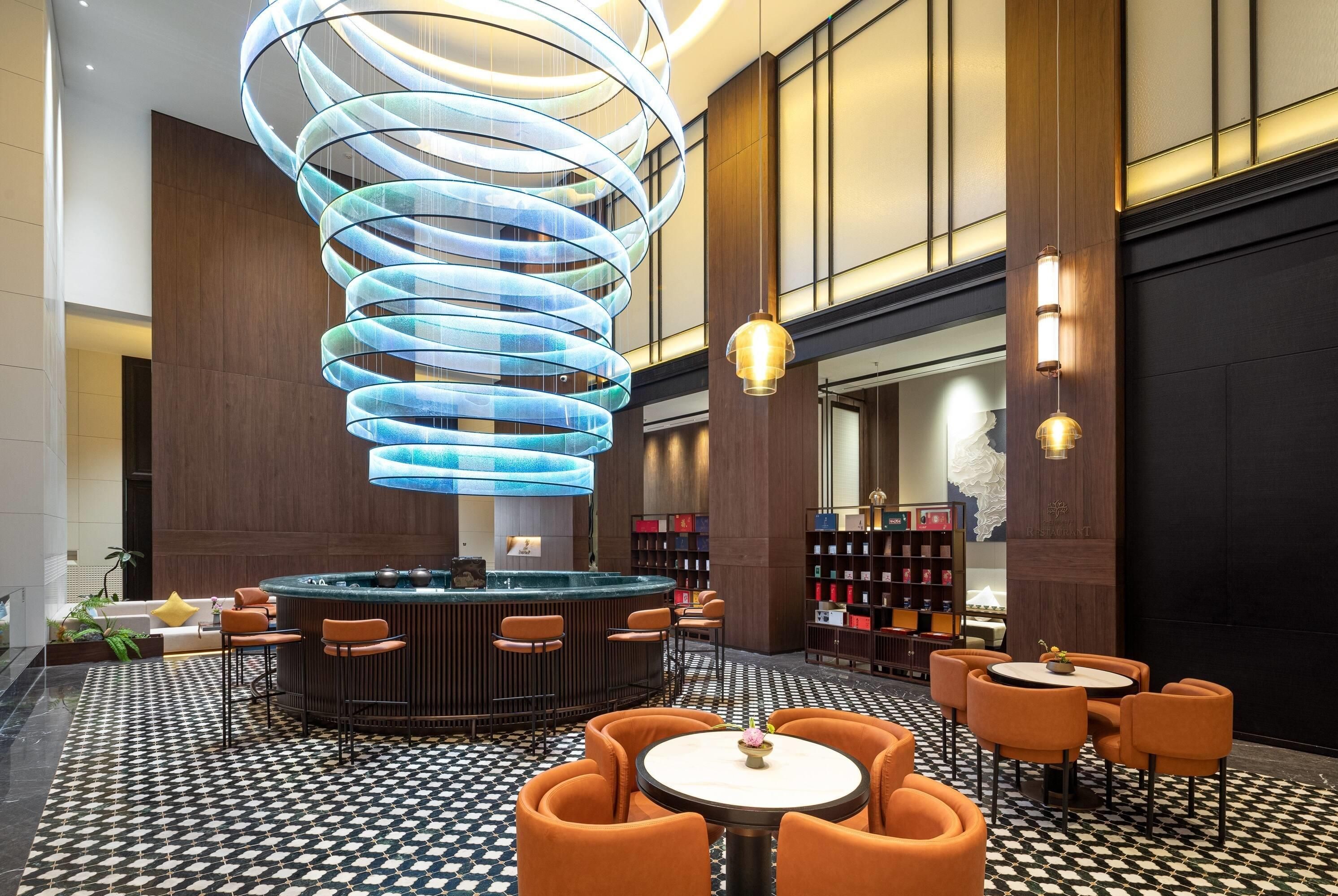 A modern lobby with a central circular seating area, a spiral light fixture, and a reception desk.