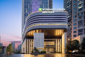 A modern hotel with a curved facade, illuminated signage, and a prominent entrance. - Wyndham Garden Changsha Economic Development Zone (Changsha)