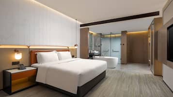 A modern hotel room with a large bed, bedside table with a phone, and a bathroom with a bathtub and shower.