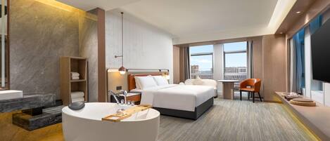 Una habitación de hotel moderna con una cama grande, un área de descanso con una mesa redonda, un baño con bañera y vistas a la ciudad por la ventana.