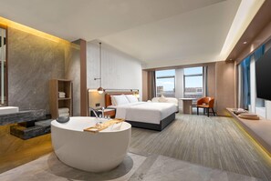 A modern hotel room with a large bed, a sitting area with a round table, a bathroom with a bathtub, and a city view through the window. - Wyndham Garden Changsha Economic Development Zone (Changsha)