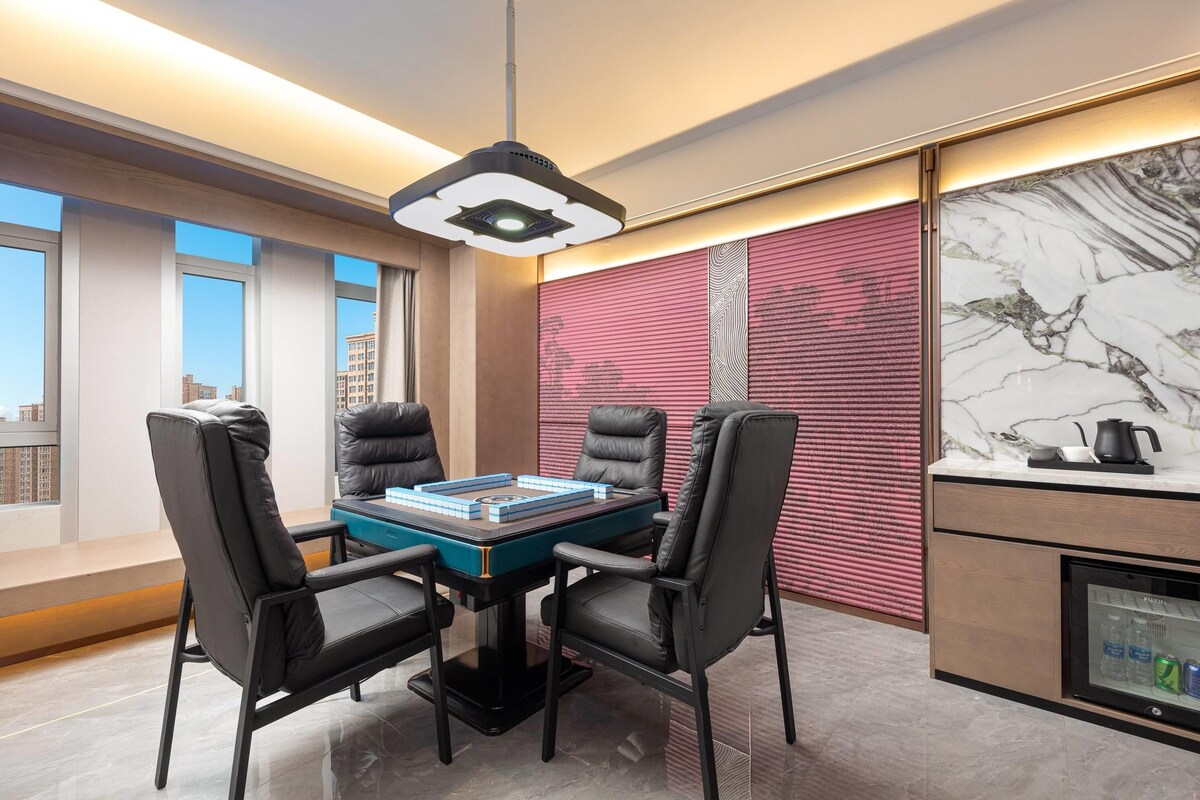 A modern dining area with a table set for four, surrounded by leather chairs, a ceiling light fixture, and a view of the cityscape through large windows.