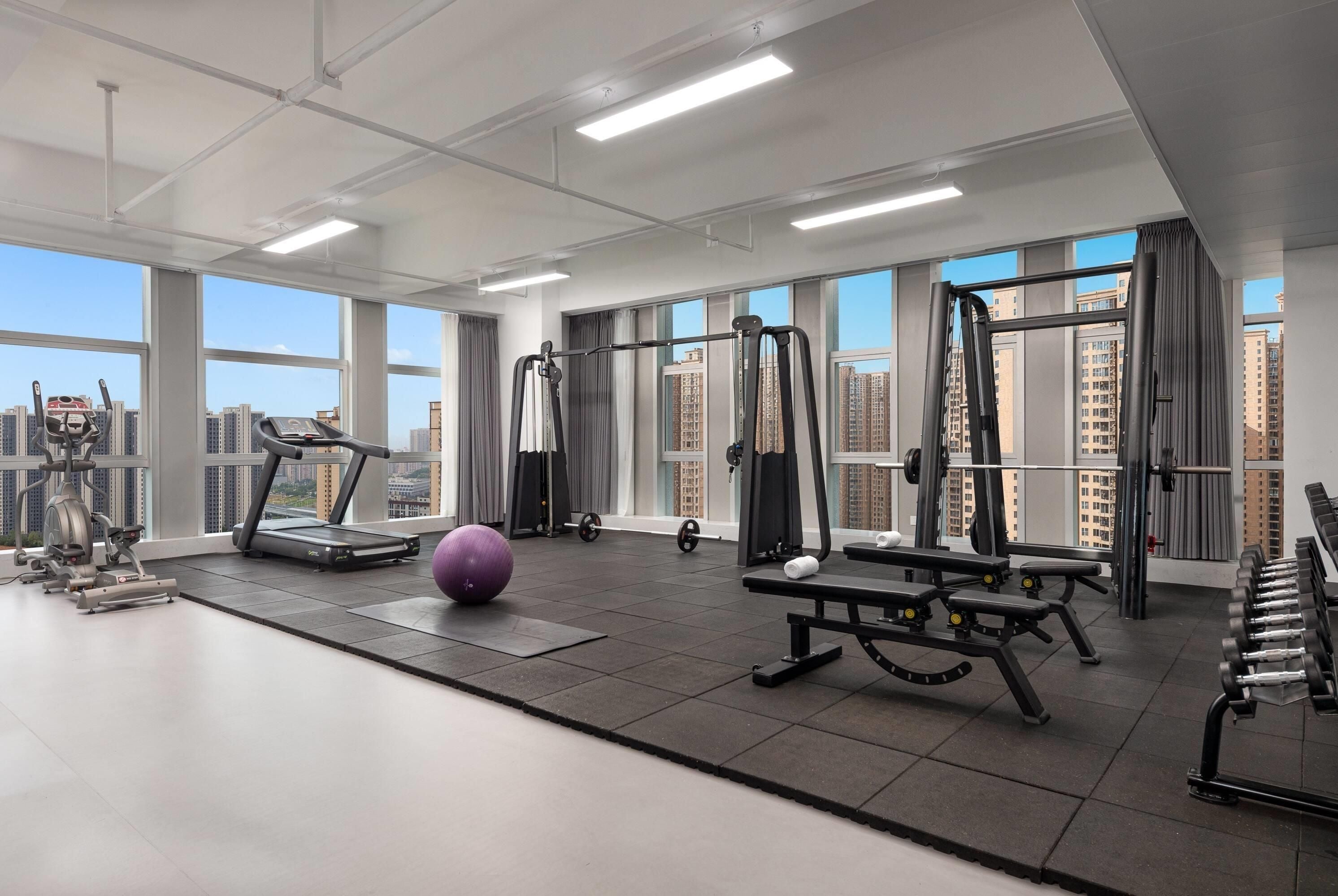 A gym with exercise equipment, a treadmill, and a large window with a city view.